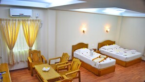 Habitación de hotel con dos camas individuales, una mesa de madera con sillas, un equipo de aire acondicionado y una ventana con cortinas.