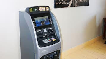An ATM machine in a room with a tiled floor and a cityscape painting on the wall.