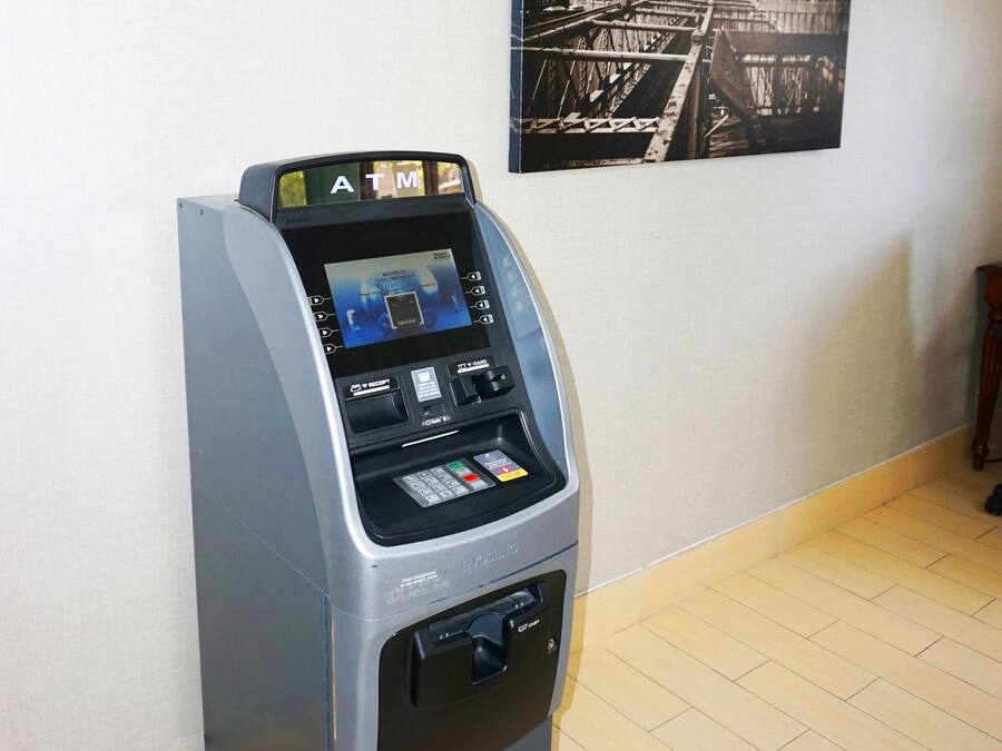 An ATM machine in a room with a tiled floor and a cityscape painting on the wall.