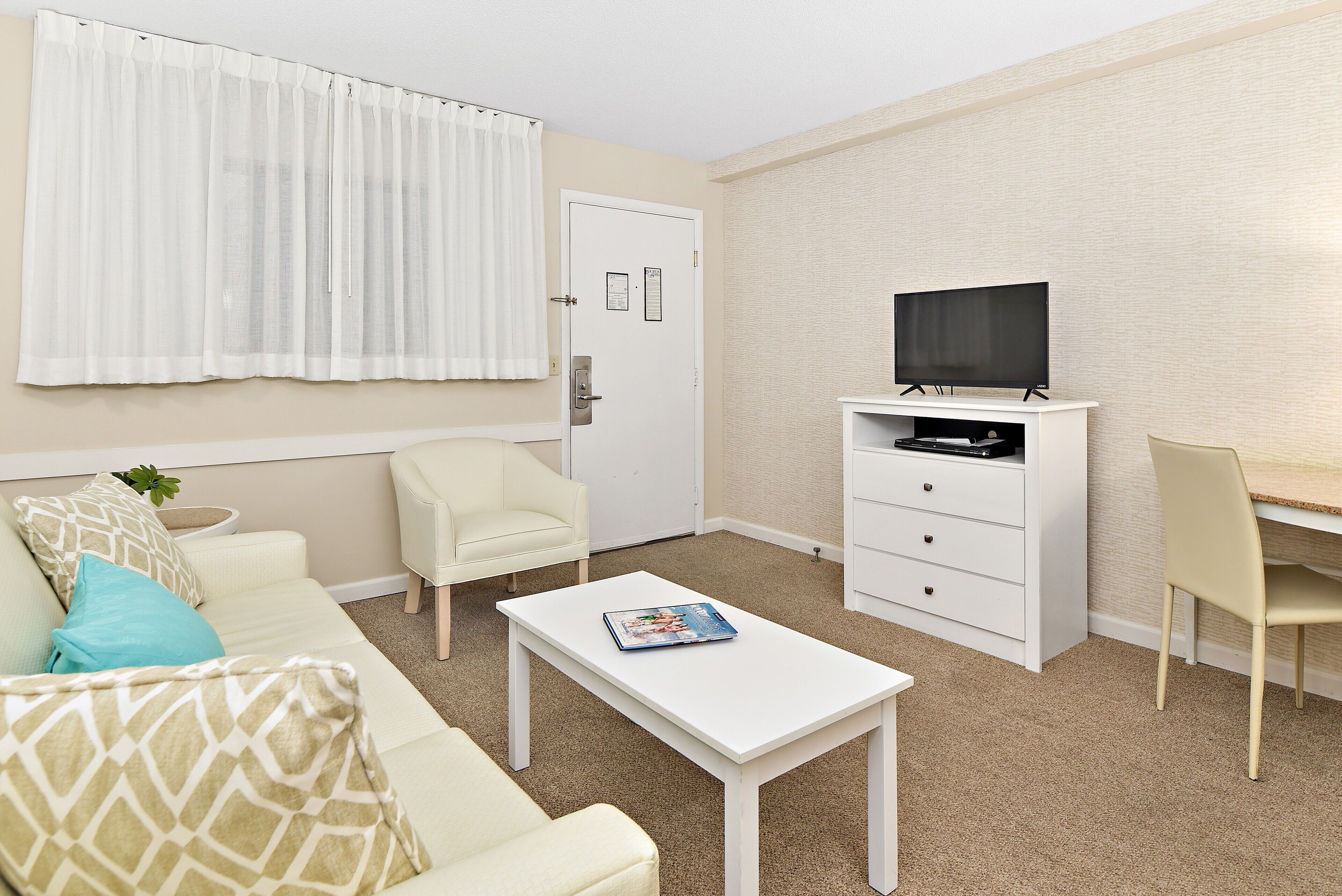 A modern living room with a white sofa, a coffee table, a TV on a white stand, and a door with a sign.