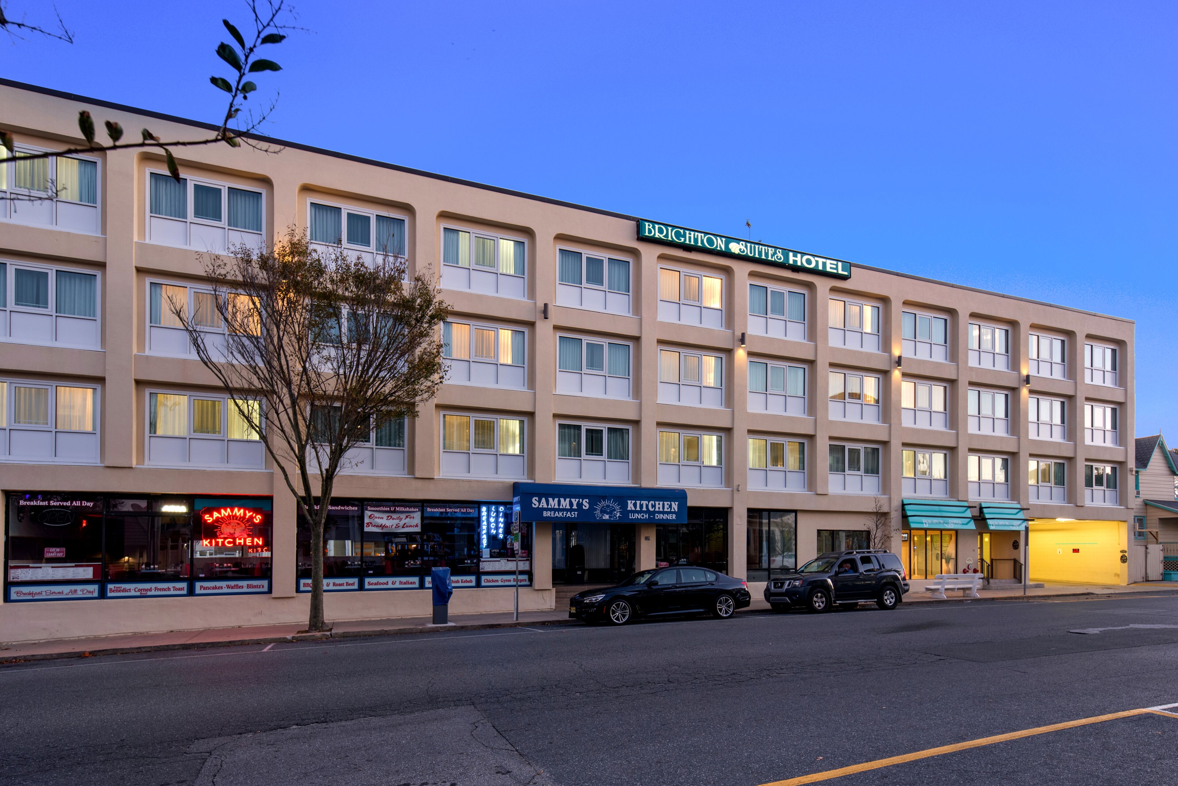 Un hotel con varios pisos, un cartel que dice 'Brighton Suites Hotel' y un restaurante cercano llamado 'Sammy's Kitchen'.