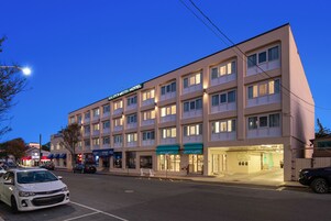 Un hotel de varios pisos con fachada plana, varios balcones y entrada a nivel de calle.