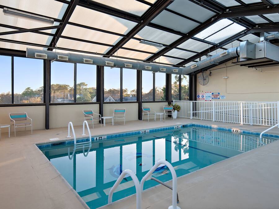 An indoor swimming pool with clear glass walls, a pool ladder, and several lounge chairs.