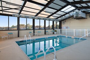 An indoor swimming pool with clear glass walls, a pool ladder, and several lounge chairs.