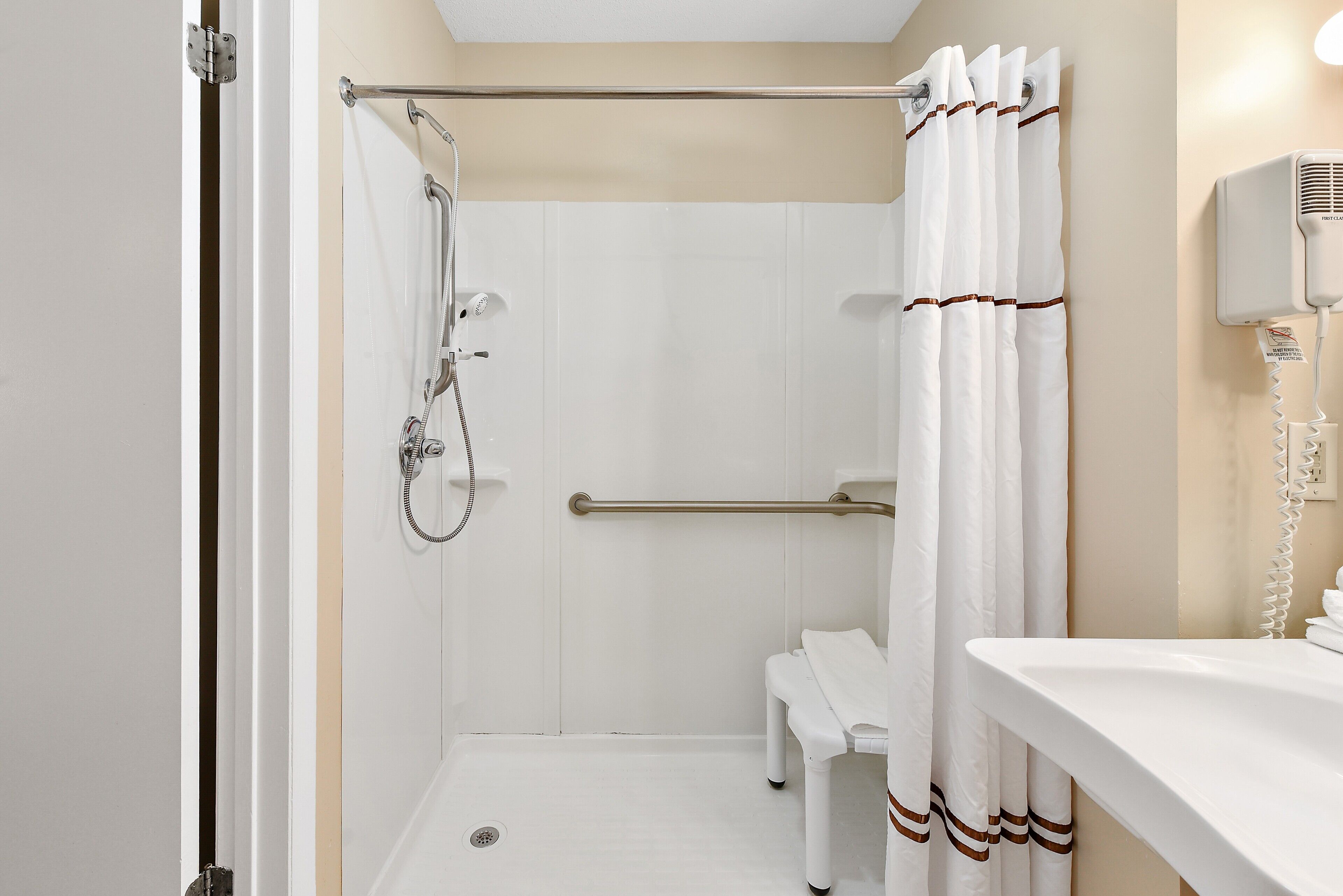 A bathroom with a shower, a bench, and a hand dryer.