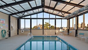 An indoor swimming pool with clear views of the cityscape through large windows. - Brighton Suites Hotel (Rehoboth Beach)