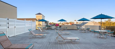 An outdoor deck with lounge chairs and tables, umbrellas, and a white fence.