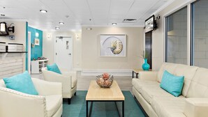 A modern living room with a beige sofa, a white armchair, and a coffee table. There is a framed artwork on the wall and a vase with a plant on a side table. - Brighton Suites Hotel (Rehoboth Beach)
