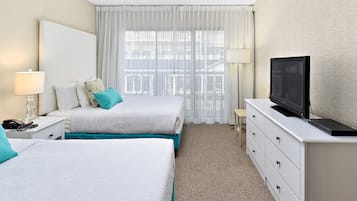 Ein Hotelzimmer mit zwei Betten, einem Fernseher, einem Schreibtisch mit Lampe und Blick ins Freie durch transparente Vorhänge.