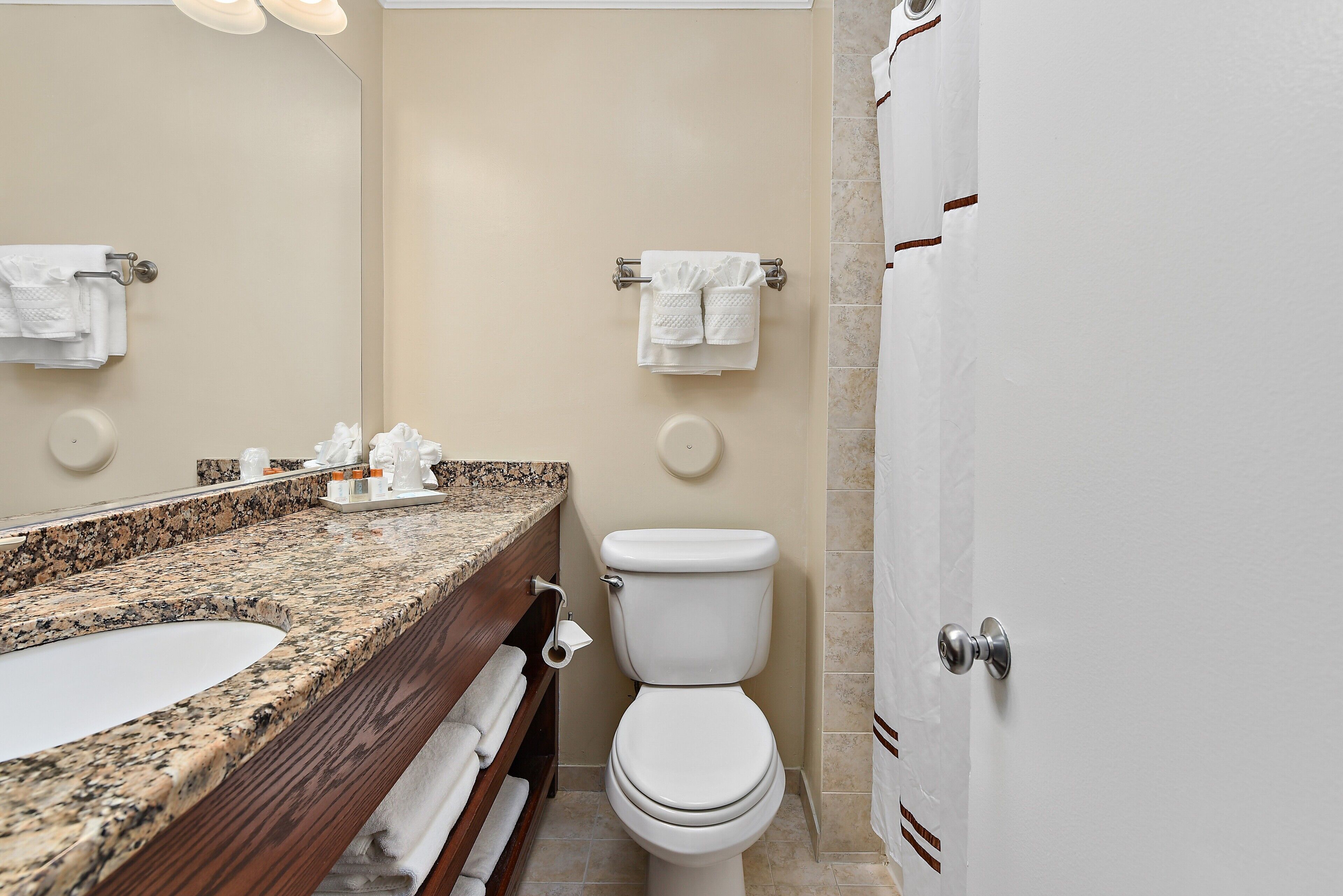 A bathroom with a granite countertop sink, a toilet, and a mirror.