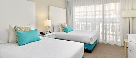 A hotel room with two beds, a nightstand, a lamp, and a view of the outdoors through sheer curtains.