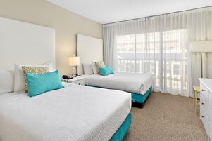 A hotel room with two beds, a nightstand, a lamp, and a view of the outdoors through sheer curtains.