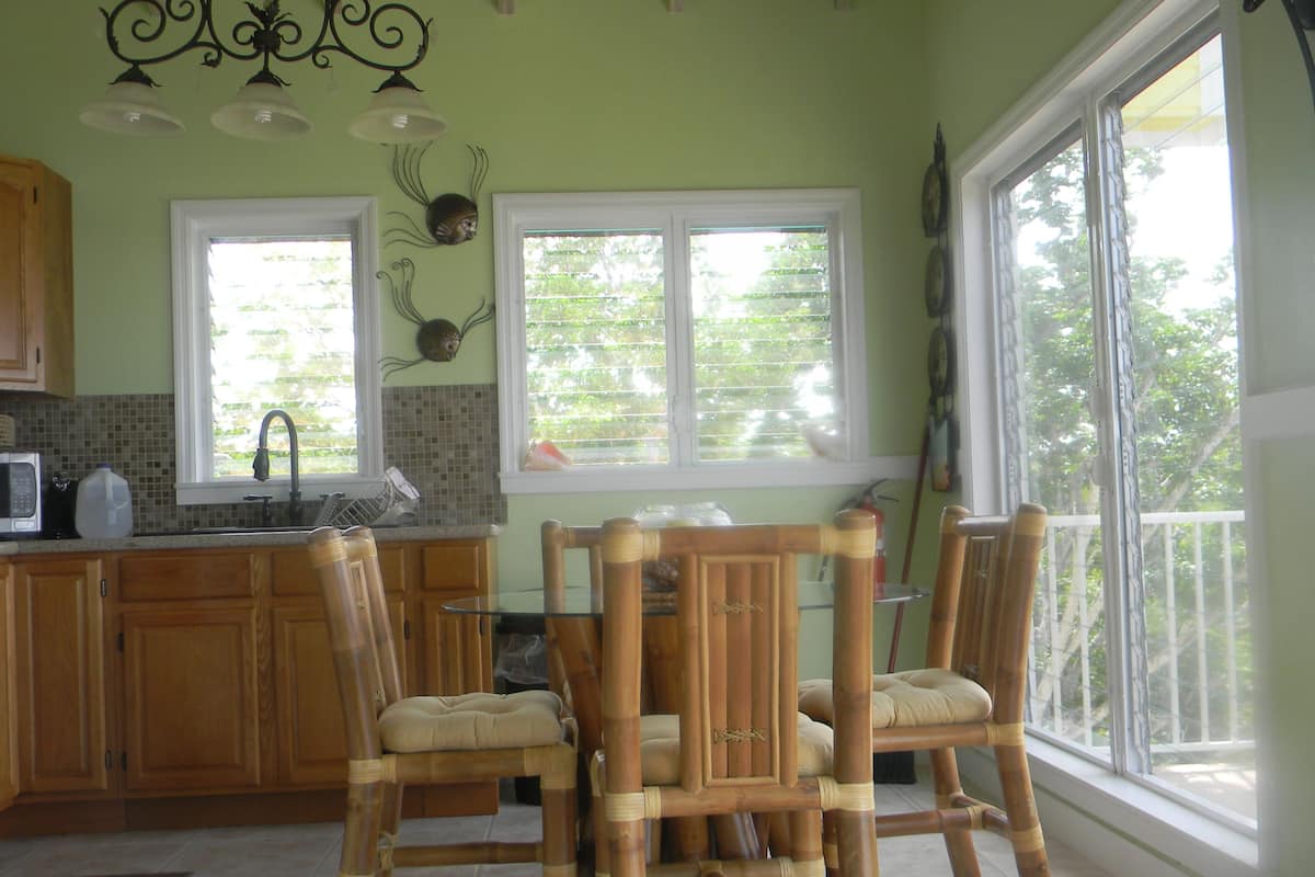 Une cuisine avec des meubles de rangement en bois, une table à manger avec des chaises et une fenêtre avec des stores.