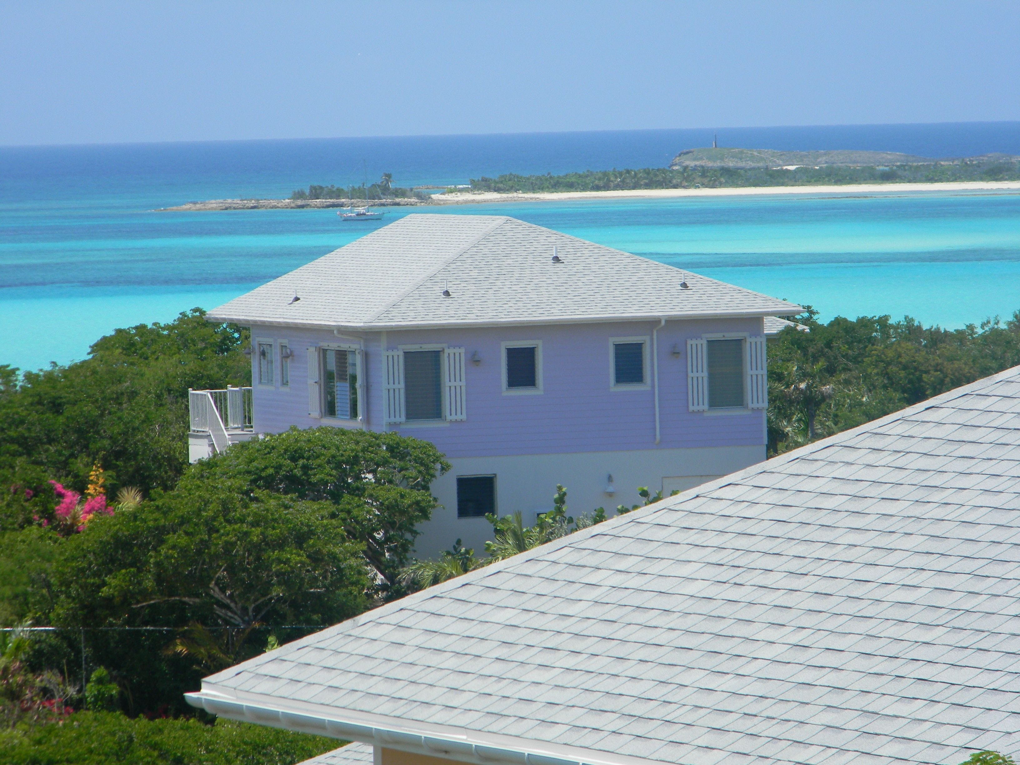 A two-story house with a flat roof, surrounded by lush greenery and a view of the ocean.