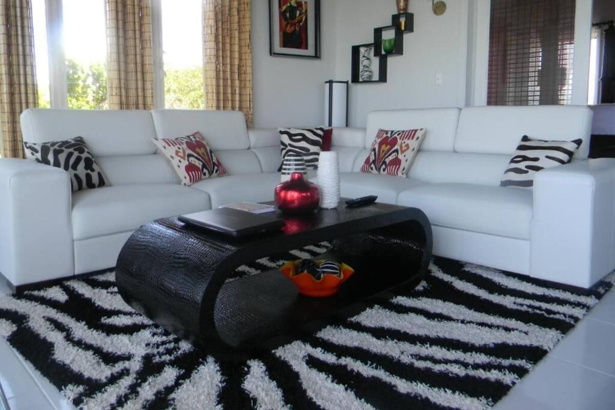 Un salon moderne avec un ensemble de canapés blancs, un tapis rayé noir et blanc et une table basse agrémentée d’objets décoratifs.
