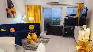 Un salon moderne avec un canapé bleu, un fauteuil blanc, une table en verre et un meuble TV noir.
