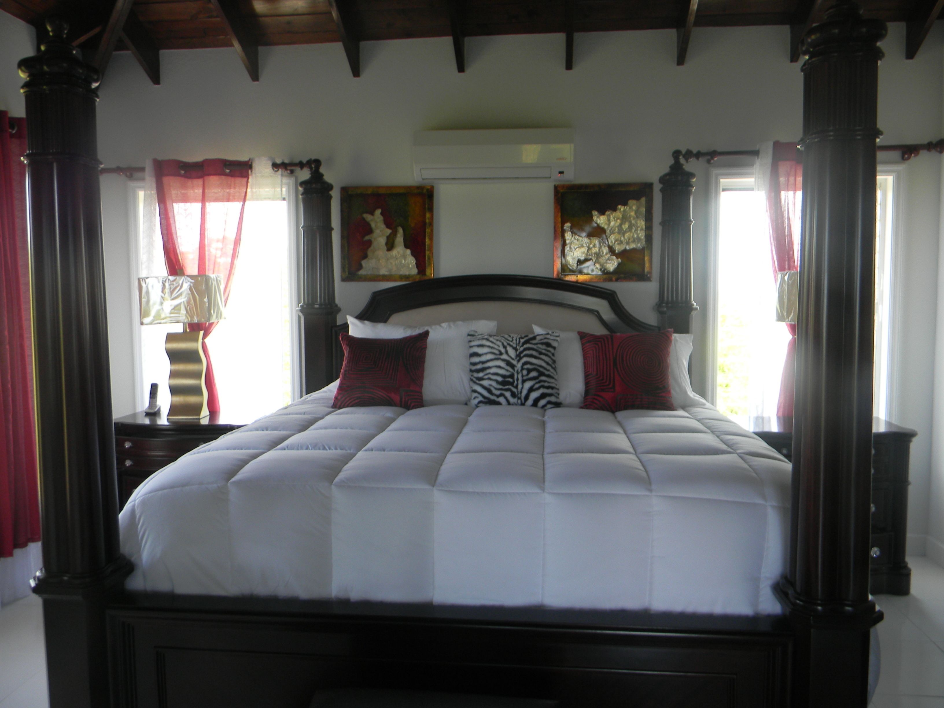 Una cama grande con estructura de madera oscura, ropa de cama blanca y varias almohadas decorativas.