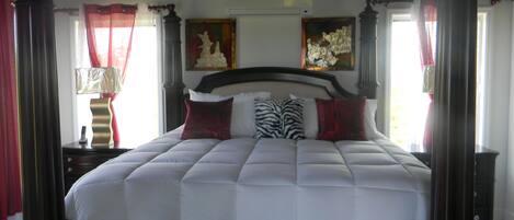Una cama grande con estructura de madera oscura, ropa de cama blanca y varias almohadas decorativas.