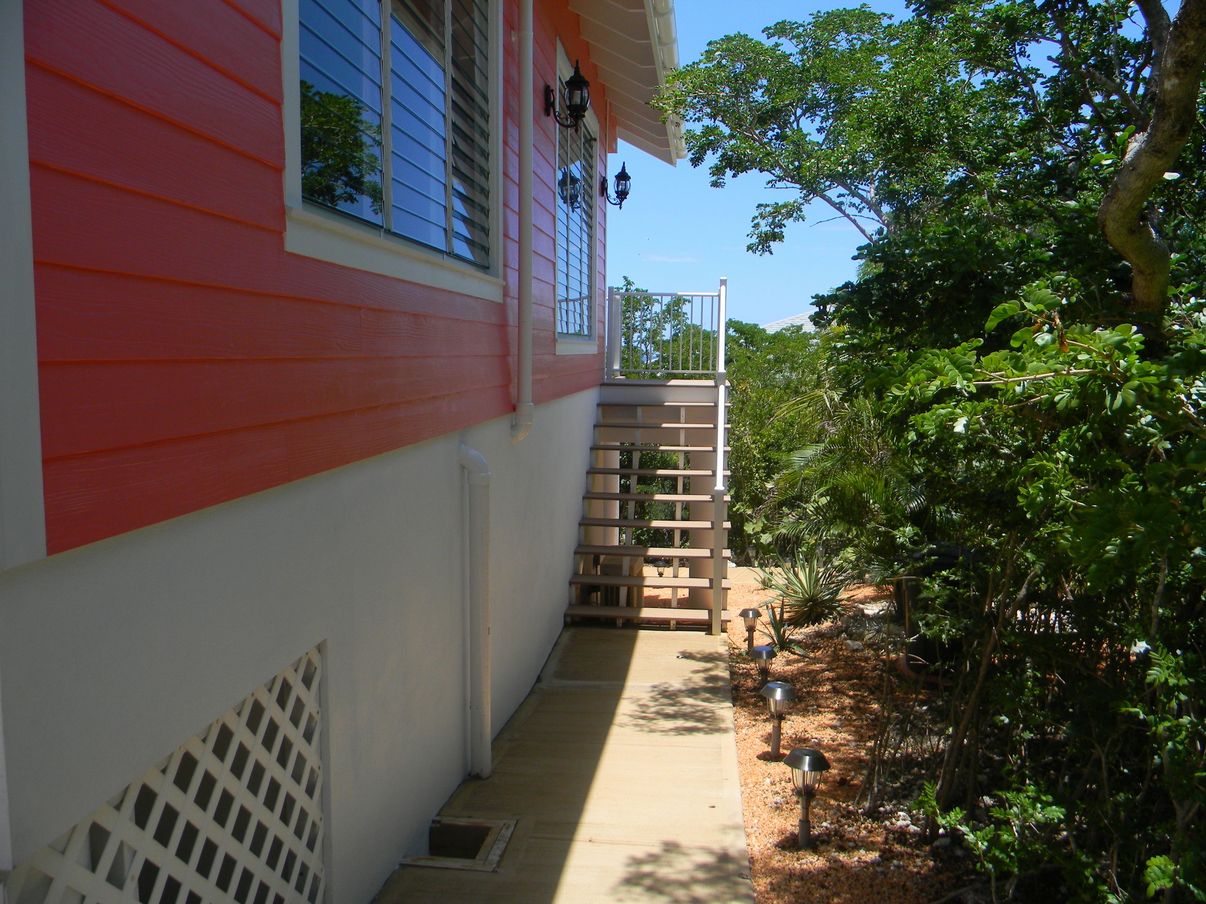 Un sendero estrecho que lleva a un edificio rojo y blanco con una pequeña escalera y una cerca de metal.