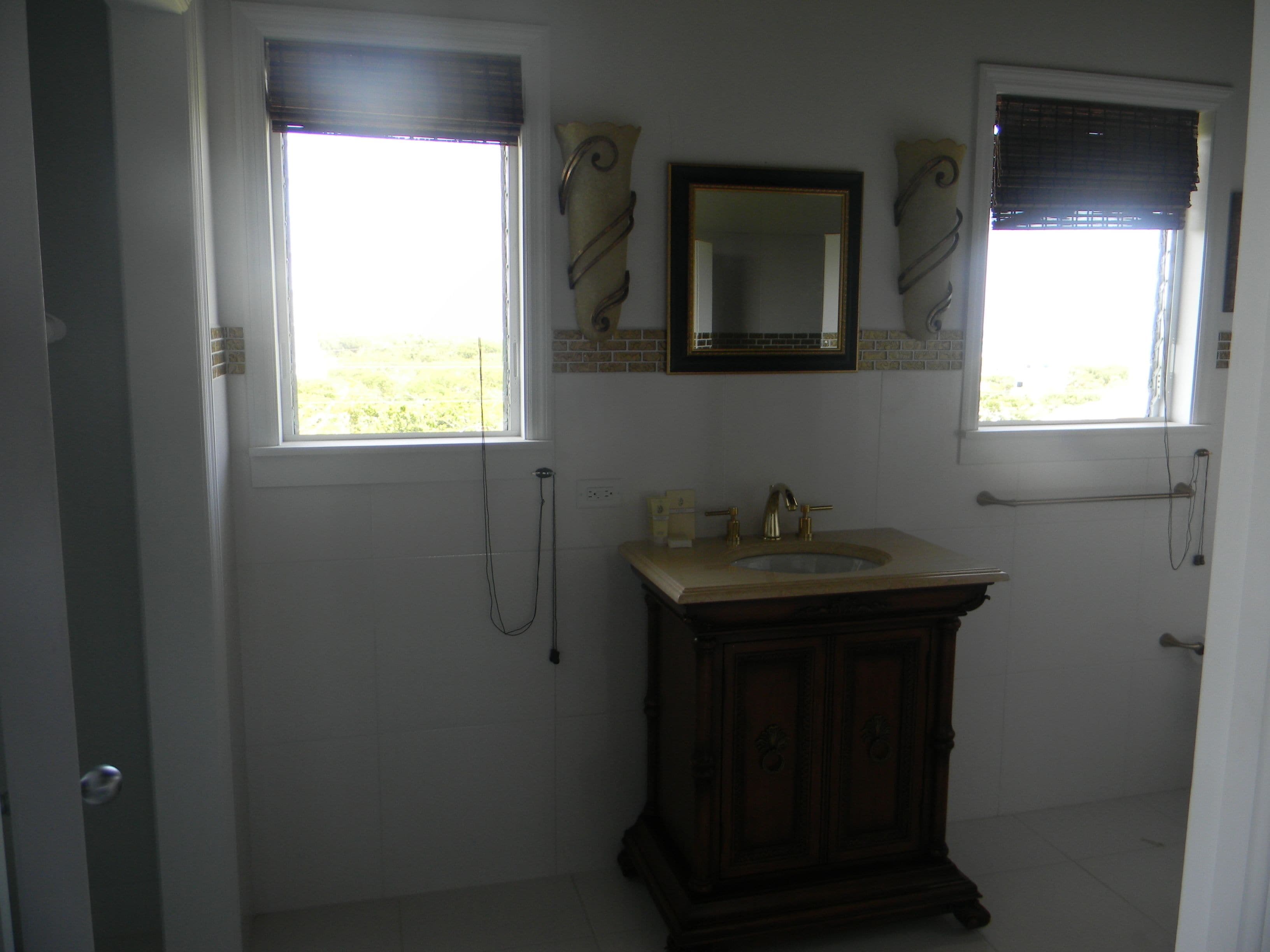 Une salle de bain avec un lavabo, un miroir et deux fenêtres équipées de stores.