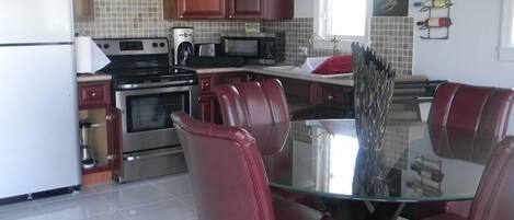 Une cuisine moderne équipée d’appareils électroménagers en acier inoxydable, de chaises en cuir rouge et d’une table à manger en verre.