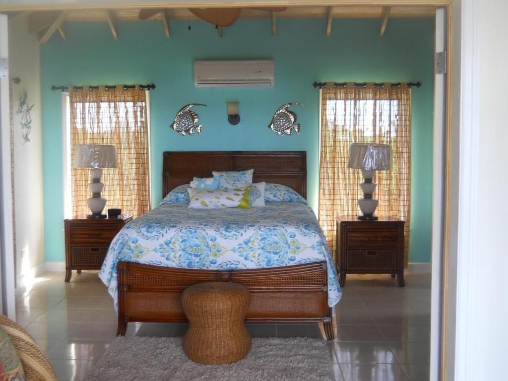 A bedroom with a large bed, two nightstands, a wicker stool, and decorative fish wall art.