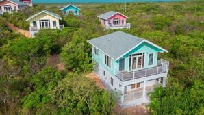 Un ensemble de petites maisons de plage colorées, à plusieurs étages et dotées de balcons, entourées d’une végétation luxuriante.