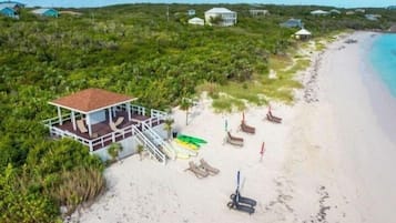 A beach house with a deck, lounge chairs, and umbrellas.