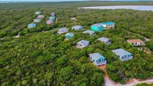 Une propriété située sur la côte, comprenant plusieurs maisons entourées d’une végétation luxuriante, avec une plage en arrière-plan.