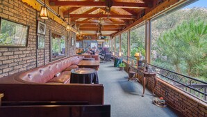 A cozy restaurant with wooden beams, brick walls, and large windows offering a view of trees. - Piazza's Pine Cone Inn (Kernville)