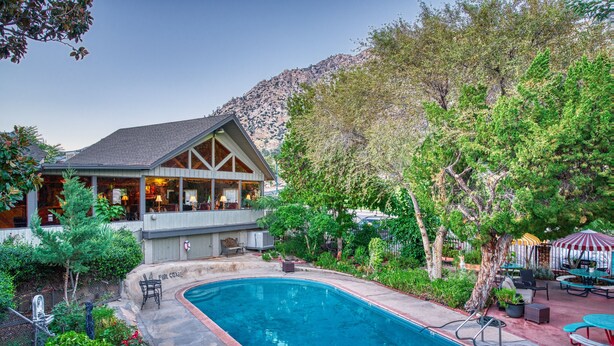 A poolside area with a pool, outdoor seating, and a building with a balcony. - Piazza's Pine Cone Inn (Kernville)