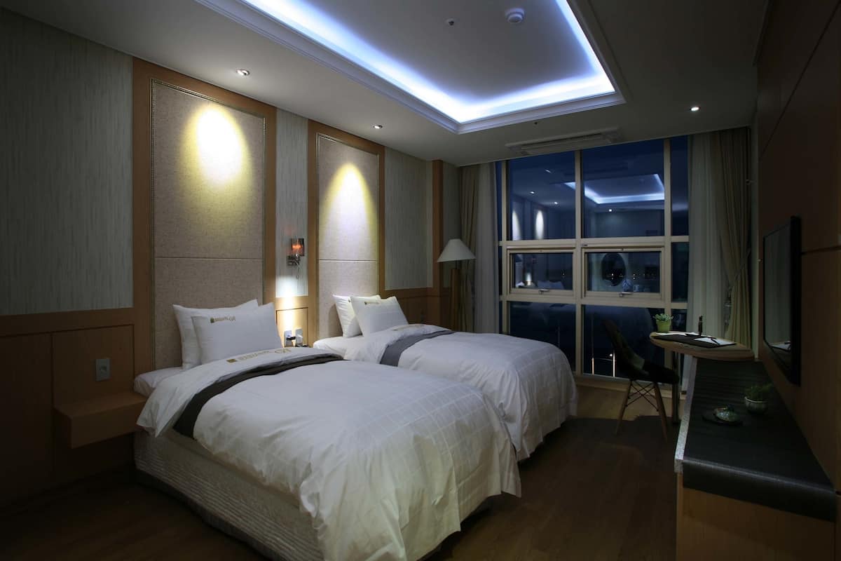 Ein Hotelzimmer mit zwei Betten, einem Schreibtisch, einem Stuhl und einem großen Fenster mit Blick auf den Nachthimmel.