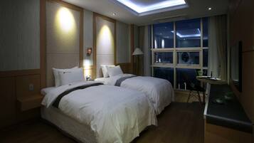 A hotel room with two beds, a desk, a chair, and a large window with a view of the night sky.