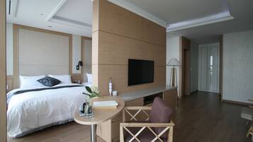 Habitació d'hotel moderna amb un llit gran, un televisor de pantalla plana penjat a la paret, una taula rodona petita amb un ram de flors i una zona de seients amb una cadira amb coixí.