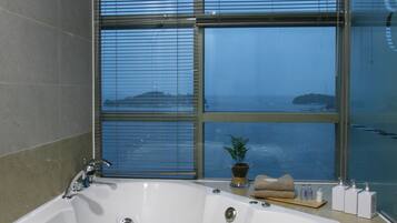 A bathroom with a large bathtub, a towel hanging on the side, and a window with a view of the sea.