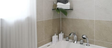A modern bathroom with a large bathtub, a towel rack with towels, and a plant.