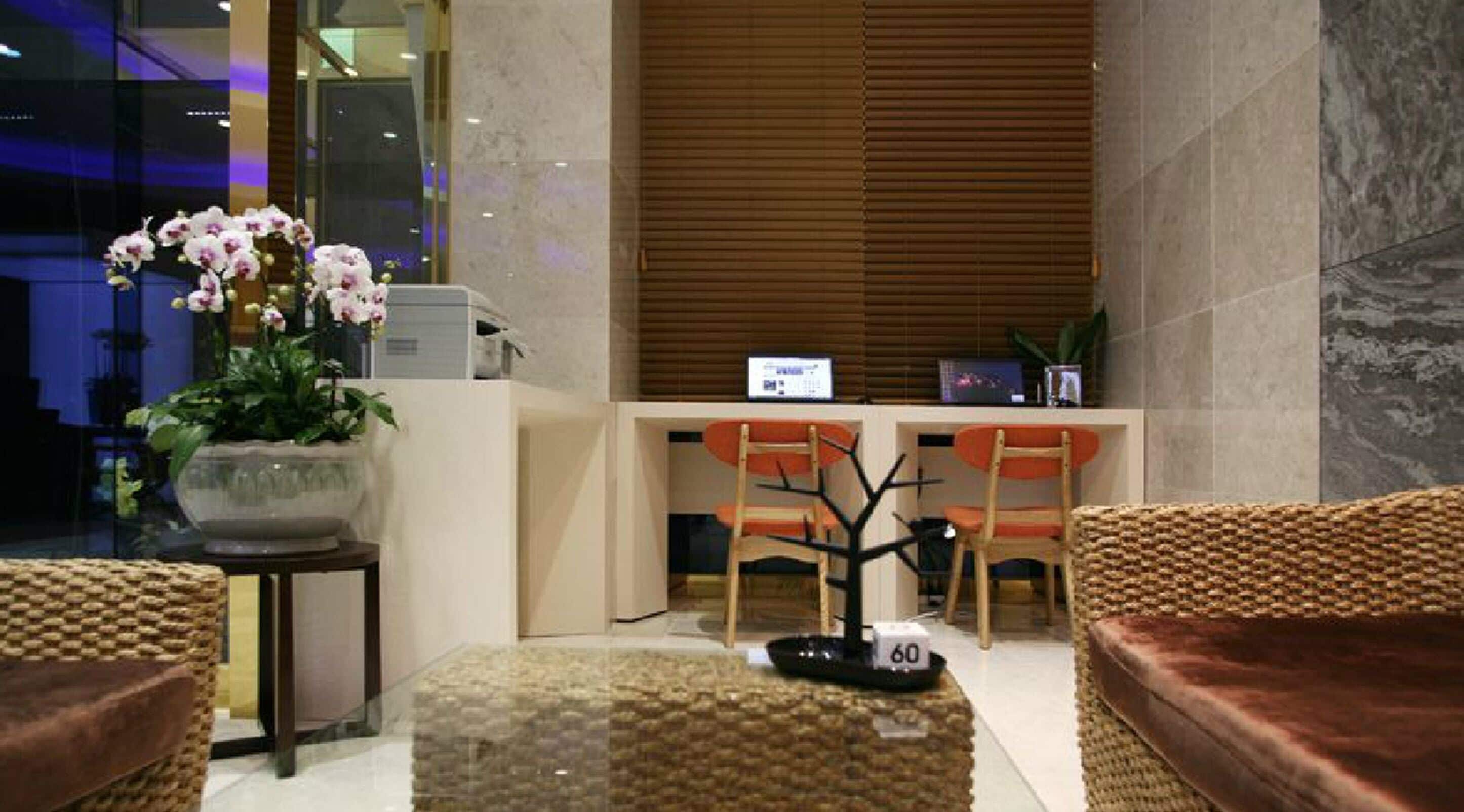 A modern lobby with a reception desk, seating area, and a potted plant.