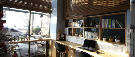 A modern kitchen with a wooden countertop, two bar stools, a laptop, and a window with blinds.