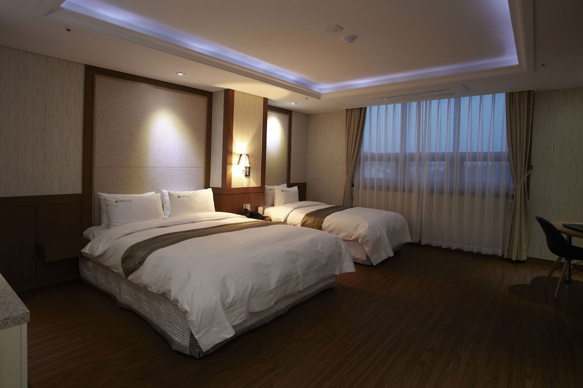 A hotel room with two beds, a desk, and a view of the city.
