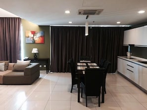 A modern living room with a sofa, a dining table with chairs, a lamp, and a painting on the wall.