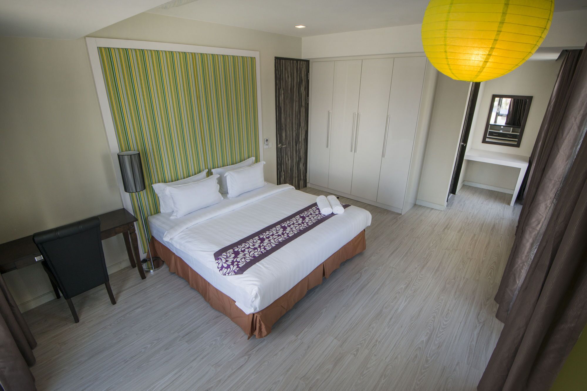 A hotel room with a bed, a desk, a wardrobe, and a hanging lamp.