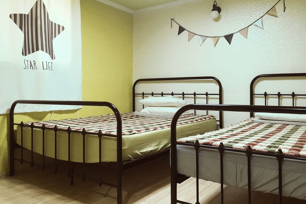 A room with two metal bunk beds, a window with curtains, a wall decoration, and a string of triangular flags.