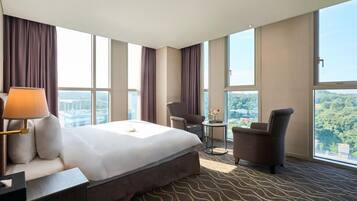 A hotel room with a large bed, a desk with a lamp, a chair, and a small table with flowers.