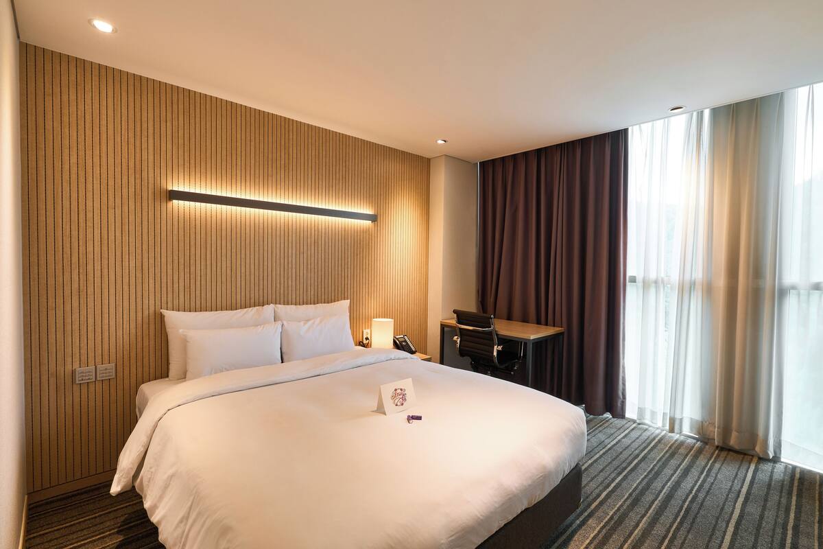 Una camera d'albergo con un letto grande, una scrivania, una lampada e vista sull'esterno.