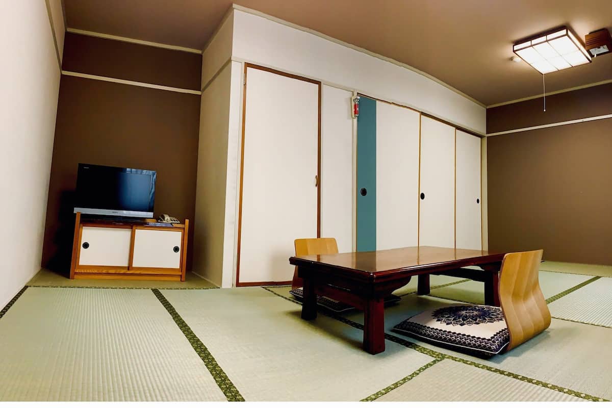 Une pièce avec un téléviseur posé sur un meuble en bois, une table avec des chaises, des tatamis et une armoire à portes coulissantes.
