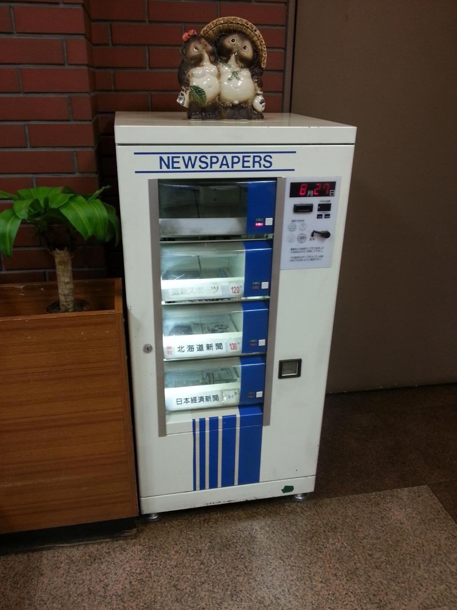 A vending machine labeled 'NEWSPAPERS' with multiple newspaper options.