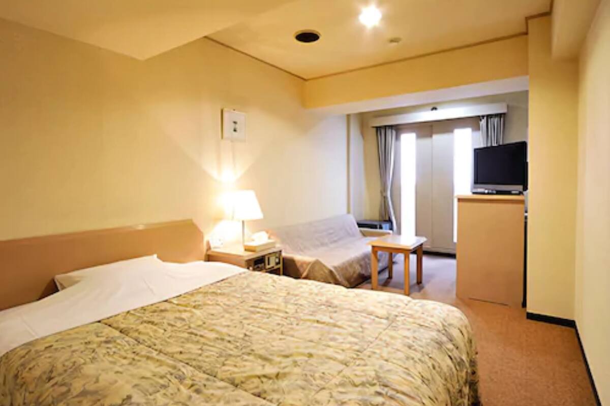 Une chambre d’hôtel avec un lit, un bureau, une télévision et une fenêtre avec des rideaux.