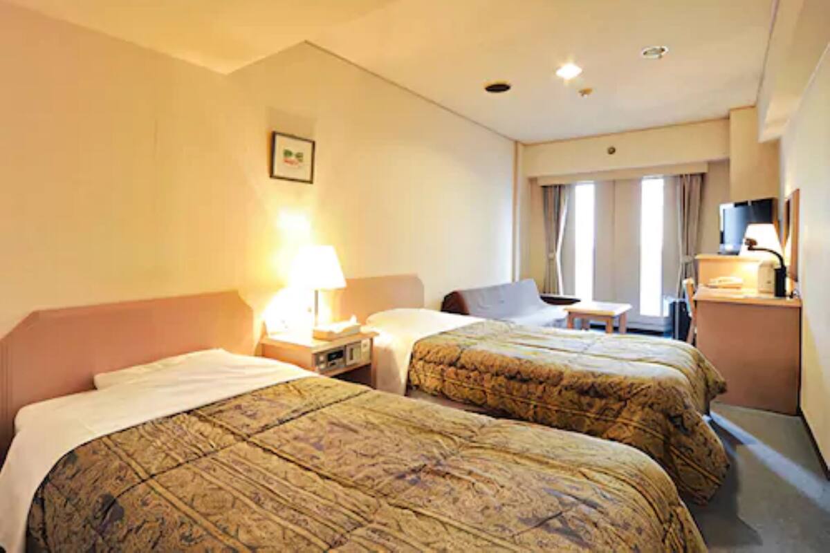 Une chambre d’hôtel avec deux lits, un bureau, une chaise, une lampe et un téléviseur.