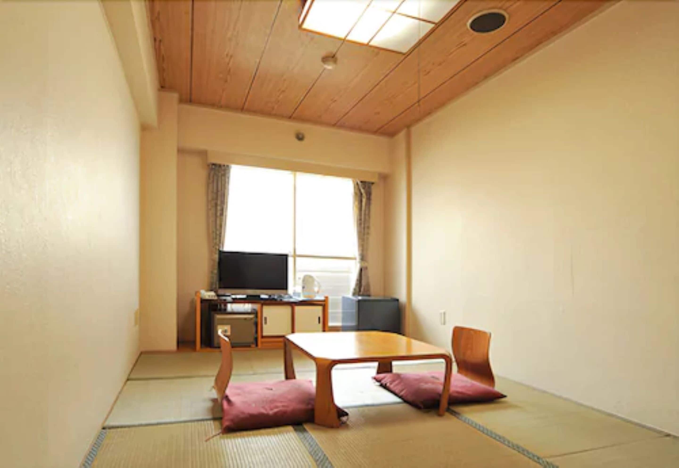 A room with tatami flooring, a low wooden table with cushions, a television, and a desk with a computer.
