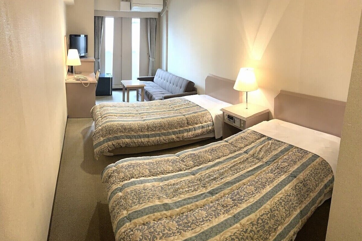 Une chambre d’hôtel avec deux lits, un canapé, une télévision et une lampe.